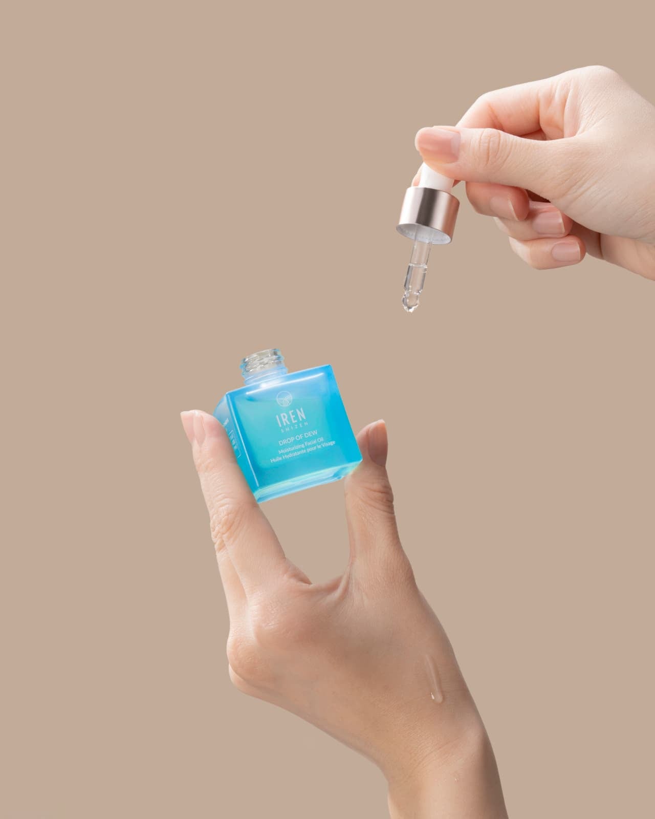 A woman's hand holding a bottle of IREN Shizen's customised Japanese skincare: DROP OF DEW Moisturizing Facial Oil. all-groups