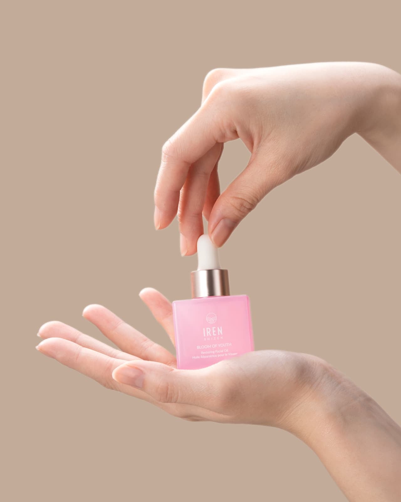 A woman's hand holding a firm BLOOM OF YOUTH Restoring Facial Oil bottle by IREN Shizen. all-groups