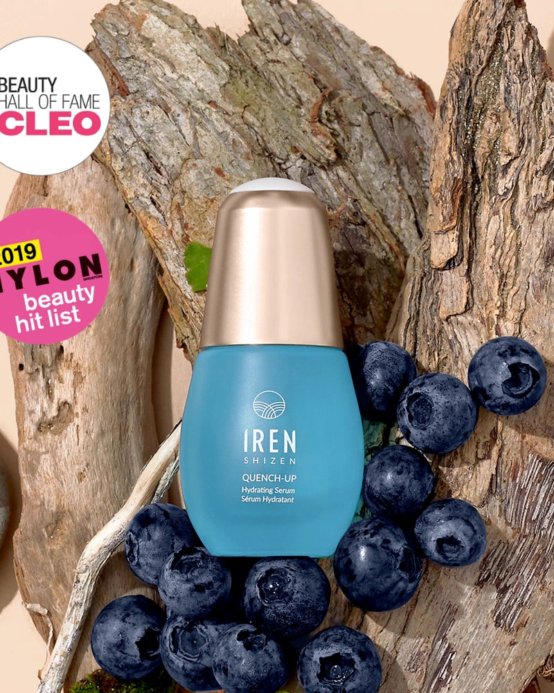 A blue bottle of IREN Shizen QUENCH-UP Hydrating Serum with hyaluronic acid is displayed on tree bark with blueberries, next to CLEO and NYLON beauty award badges. #all-groups