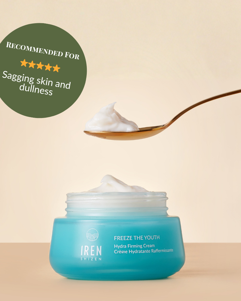 A blue jar of IRÉN Shizen's FREEZE THE YOUTH Hydra Firming Cream sits on a surface with a spoonful of cream above it. A badge reads, "Recommended for sagging skin and dullness.