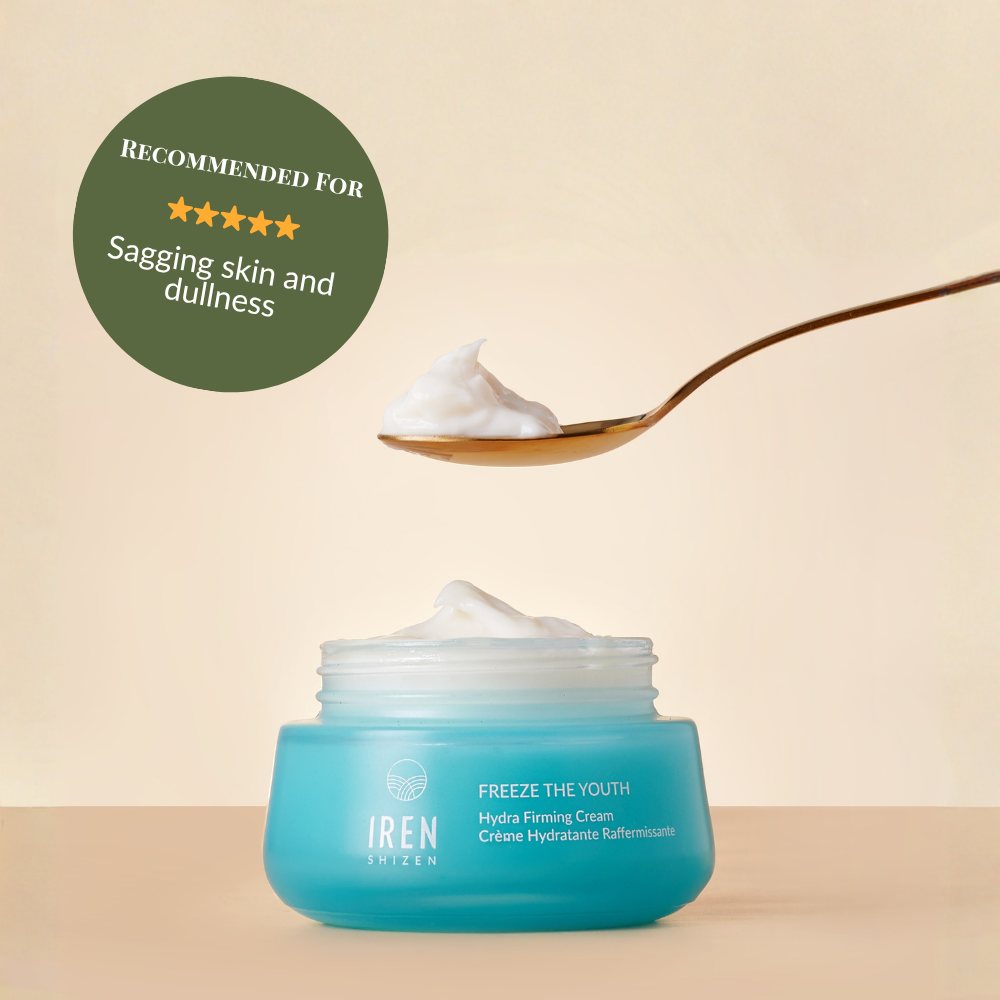 A blue jar of IRÉN Shizen's FREEZE THE YOUTH Hydra Firming Cream sits on a surface with a spoonful of cream above it. A badge reads, "Recommended for sagging skin and dullness.