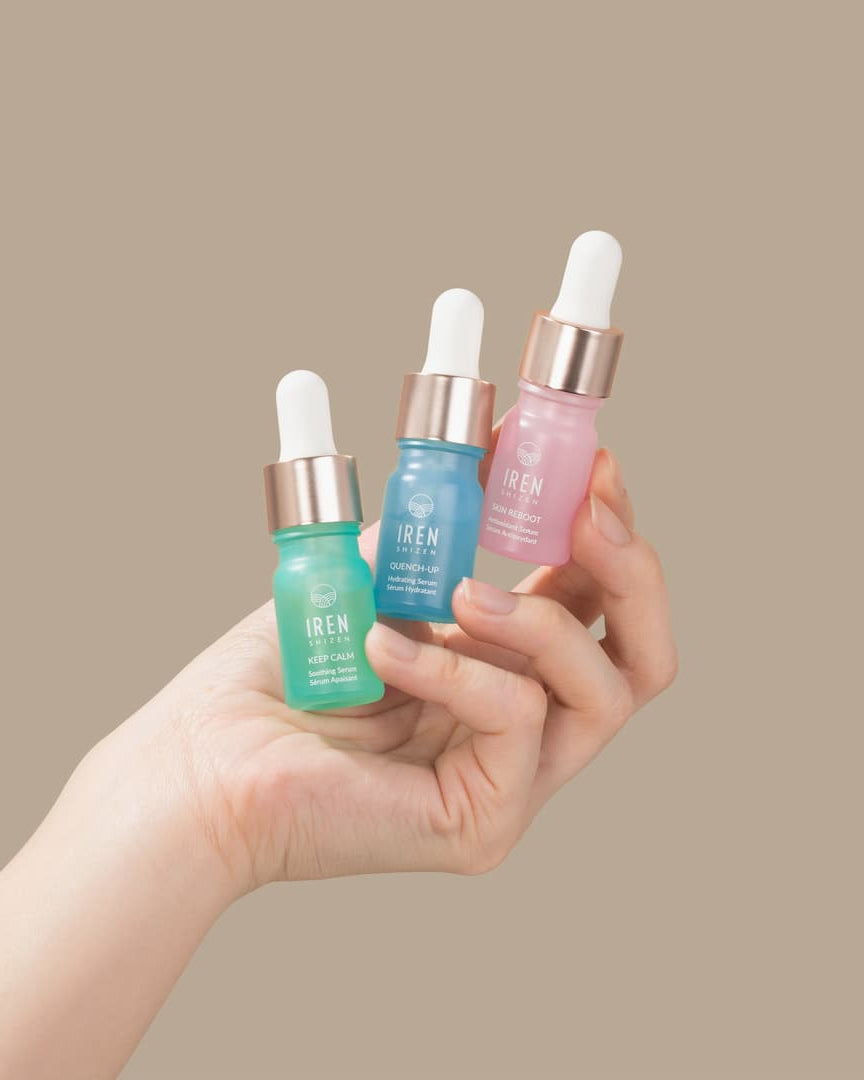 A woman's hand holding three DEW UP Hydrating Discovery Kit minis, each formulated to provide hydration and promote skin-healing from IREN Shizen.