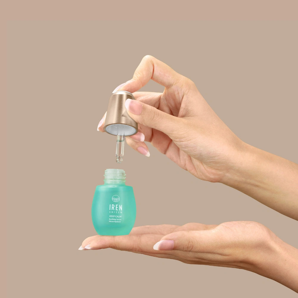 A person dispenses KEEP CALM Soothing Serum by IREN Shizen from a dropper bottle onto their palm against a plain beige background. #all-groups