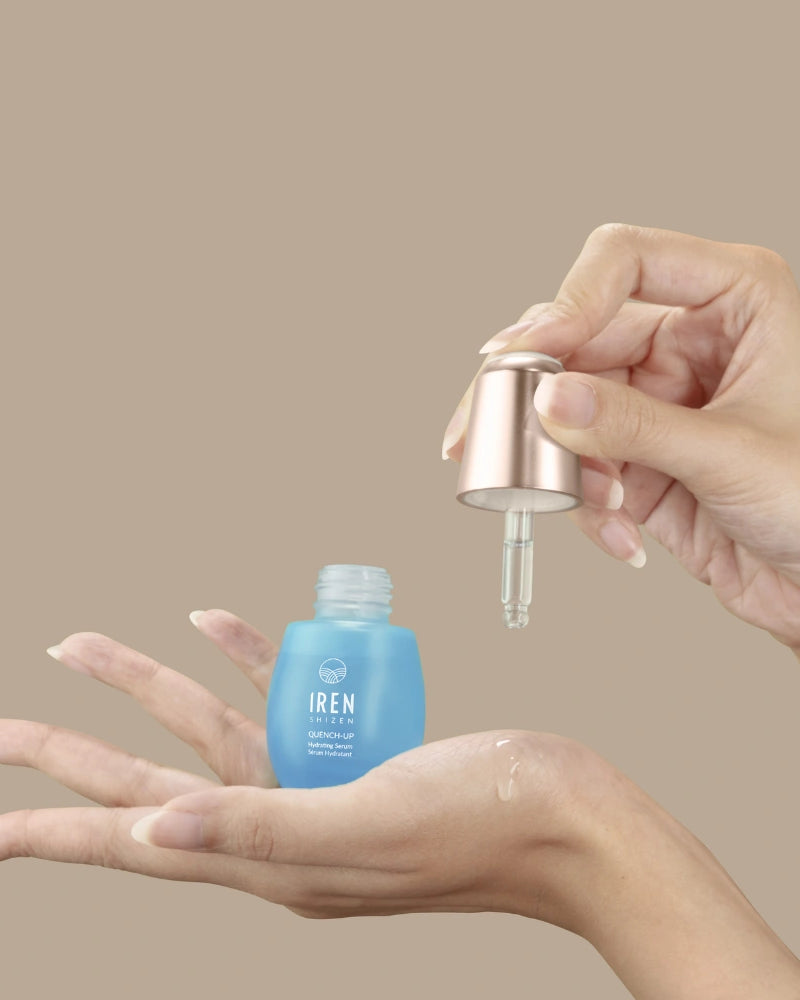 A hand holds an open blue QUENCH-UP Hydrating Serum bottle by IREN Shizen while another dispenses hyaluronic acid with a dropper onto the palm, promising plump skin against a beige background.
#all-groups