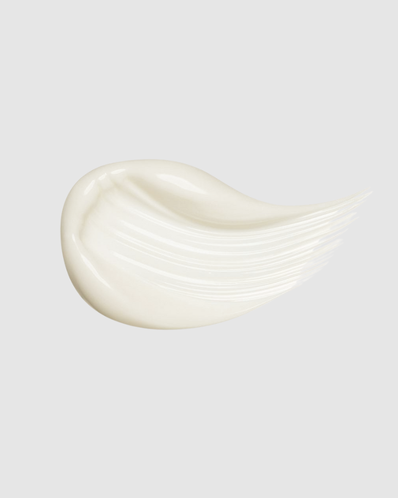 The TIMELESS ELIXIR Multi-Lift Eye and Lip Cream from IREN Shizen, a creamy white substance infused with bakuchiol for anti-aging benefits, is smeared smoothly against a light gray background.