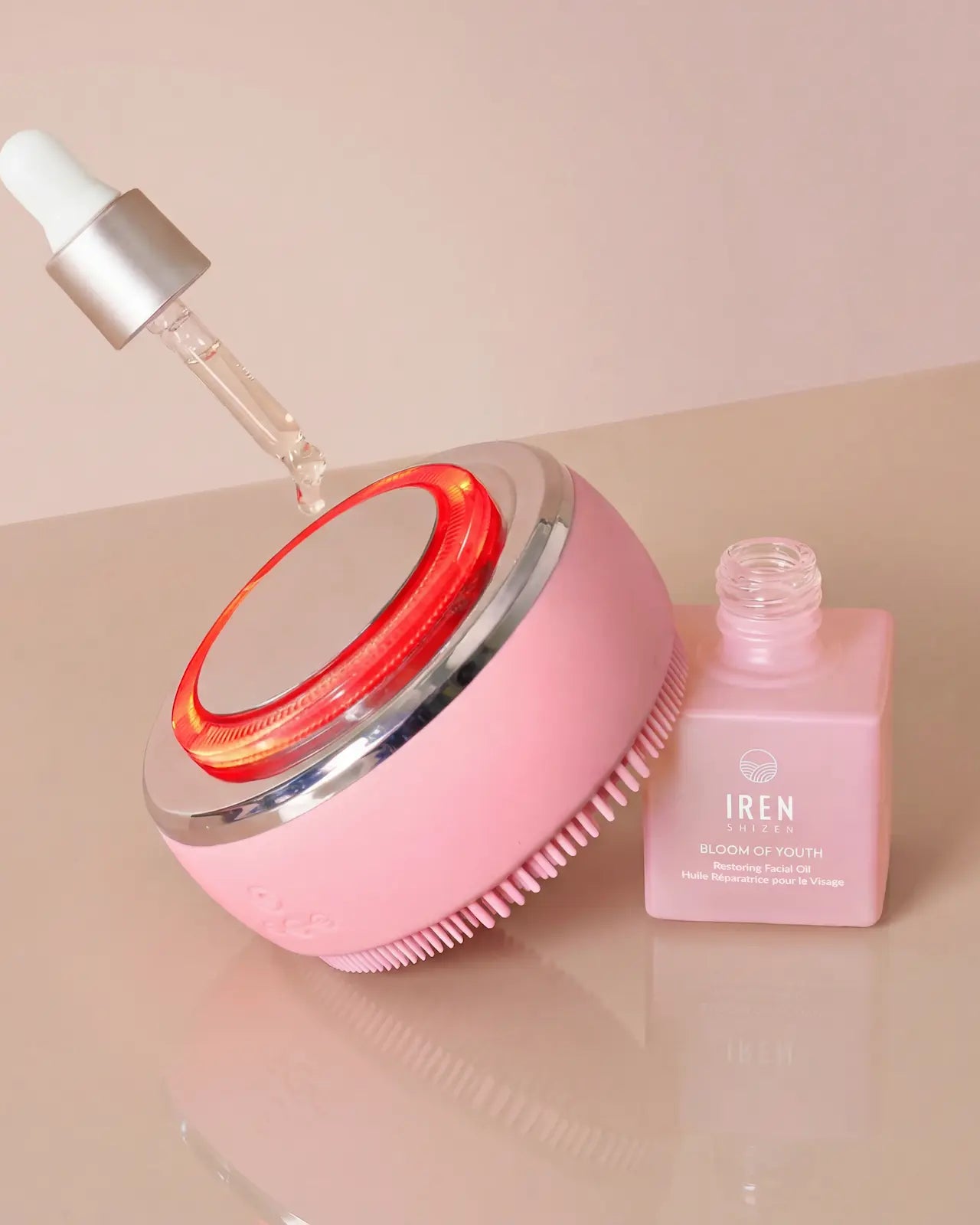 The IREN Shizen GLOW ON THE GO Travel Light Kit features a pink facial cleansing brush with LED light therapy beside a pink IRÉN Bloom of Youth serum bottle and dropper.