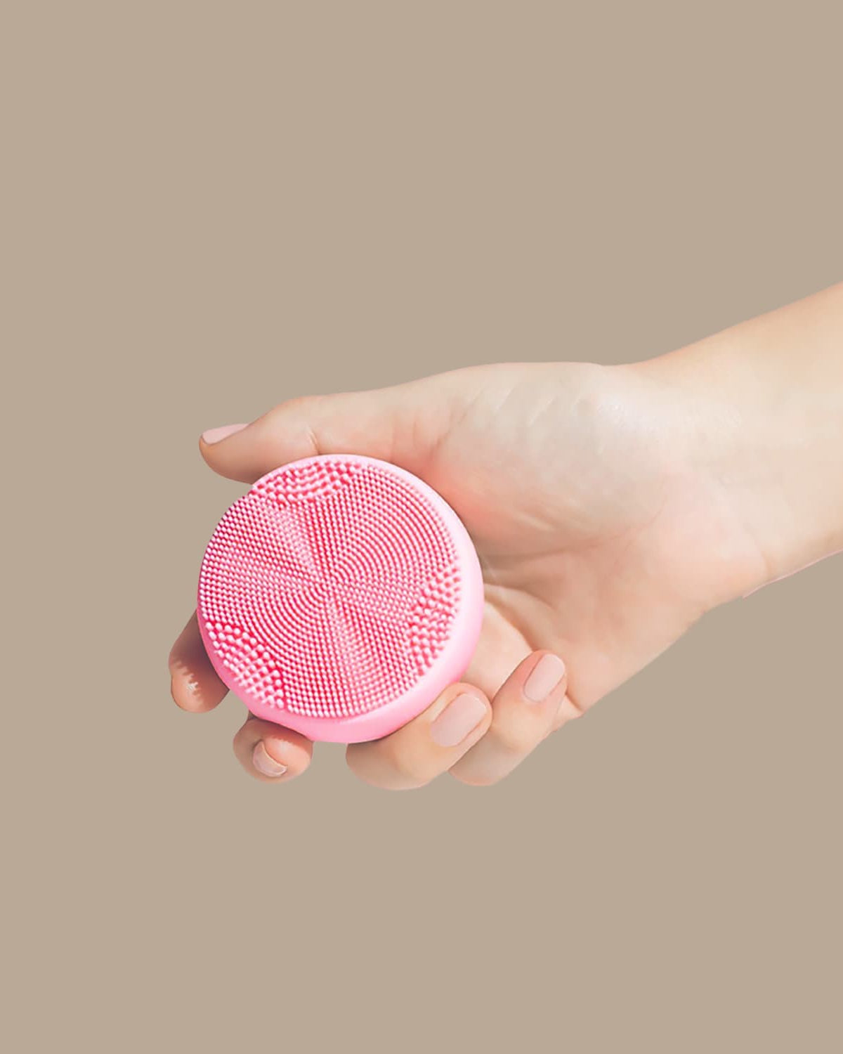 A hand holds the pink, round GLOW ON THE GO Travel Light Kit by IREN Shizen against a plain beige background—an essential for any travel skincare routine.