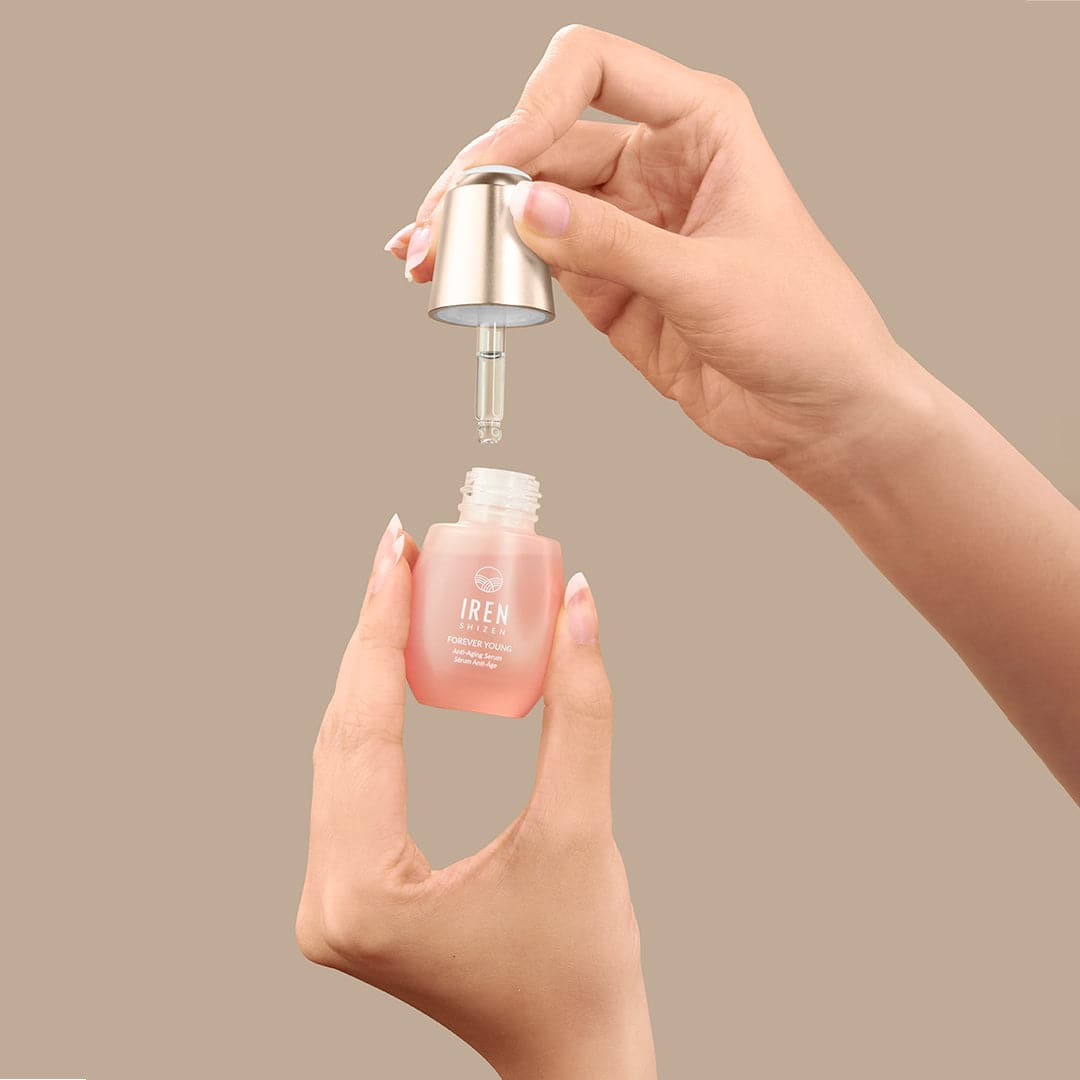 A hand is holding a bottle of IREN Shizen customised FOREVER YOUNG Anti-Aging Serum on a beige background. #all-groups