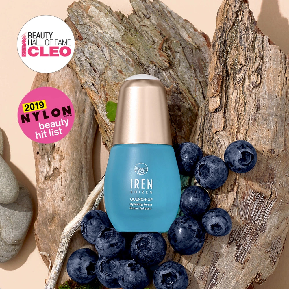 A blue bottle of IREN Shizen QUENCH-UP Hydrating Serum with hyaluronic acid is displayed on tree bark with blueberries, next to CLEO and NYLON beauty award badges. #all-groups                                                  