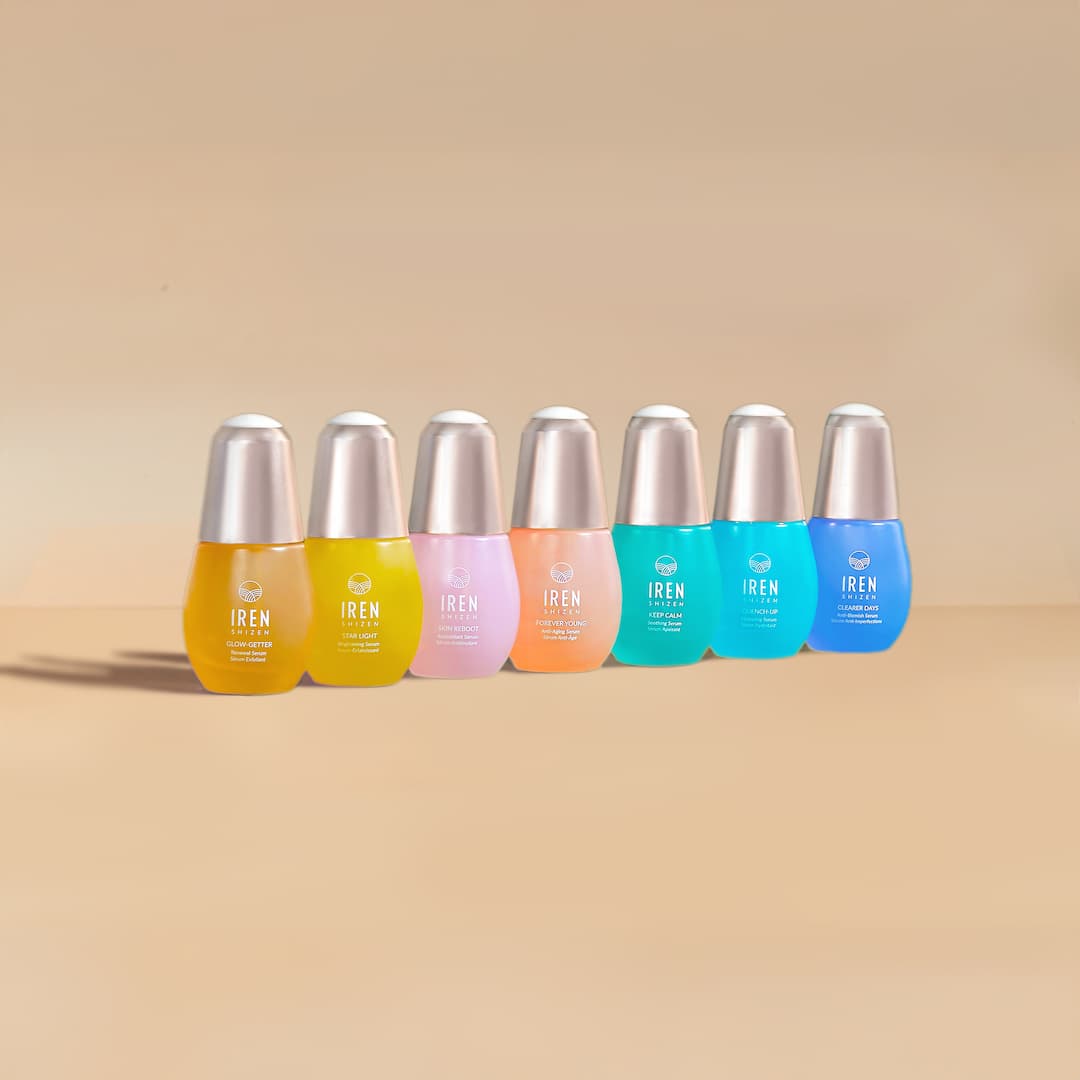 Seven colorful bottles of IREN Shizen’s MOISTURE SANDWICH Skincare Kit with silver caps are arranged in a row against a neutral background, designed to boost hydration and enhance serum absorption for radiant skin.