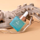 A blue dropper bottle labeled "IREN Shizen" containing DROP OF DEW Moisturizing Facial Oil for skin barrier repair rests on textured driftwood against a beige background.
#all-groups