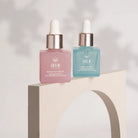 Two square IREN Shizen bottles, one pink and one blue, are displayed on a curved beige stand next to the GLOW ON THE GO Travel Light Kit, set against a neutral background.