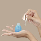 A hand holds an open blue QUENCH-UP Hydrating Serum bottle by IREN Shizen while another dispenses hyaluronic acid with a dropper onto the palm, promising plump skin against a beige background.
#all-groups