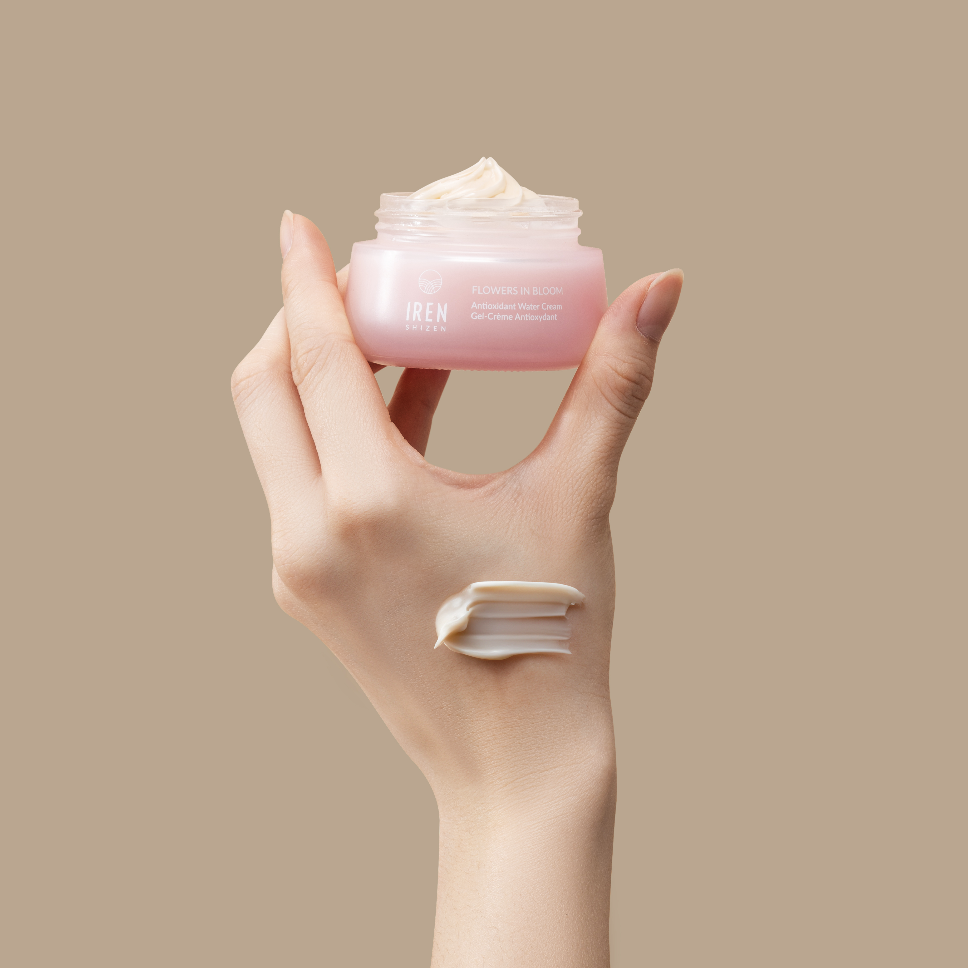 A hand holds a jar from the IREN Shizen MOISTURE SANDWICH Skincare Kit, with a swipe of cream—formulated to boost hydration and support the moisture barrier—applied to the back of the hand, set against a beige background.