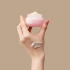 A hand holds a jar from the IREN Shizen MOISTURE SANDWICH Skincare Kit, with a swipe of cream—formulated to boost hydration and support the moisture barrier—applied to the back of the hand, set against a beige background.