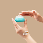 A hand holds a blue jar from the IREN Shizen MOISTURE SANDWICH Skincare Kit while another dips in; cream is swatched on the lower hand, showcasing hydration and a strengthened moisture barrier against a beige background.