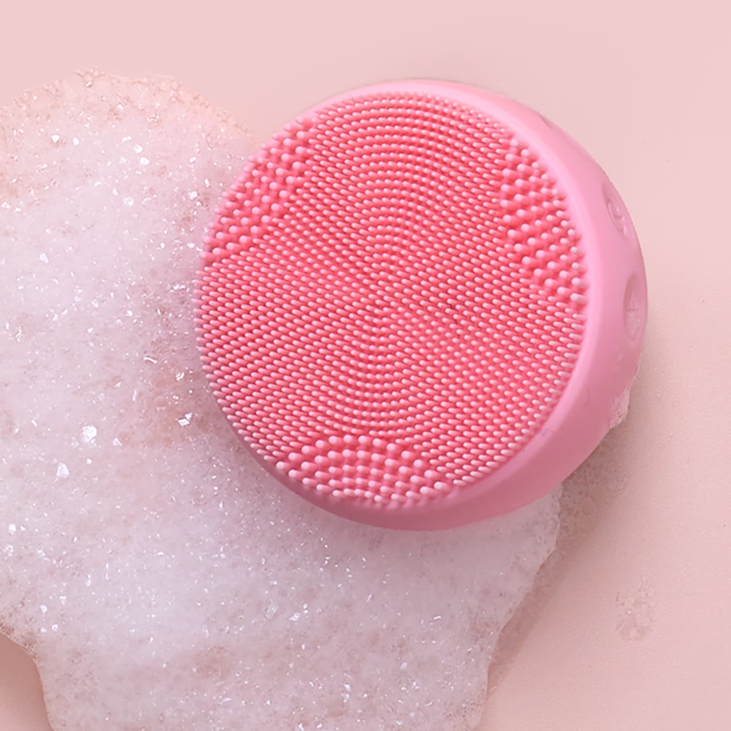 The GLOW ON THE GO Travel Light Kit by IREN Shizen features a round pink silicone cleansing device with small bristles, shown on foamy soap against a pale pink background—ideal for any travel skincare kit.
