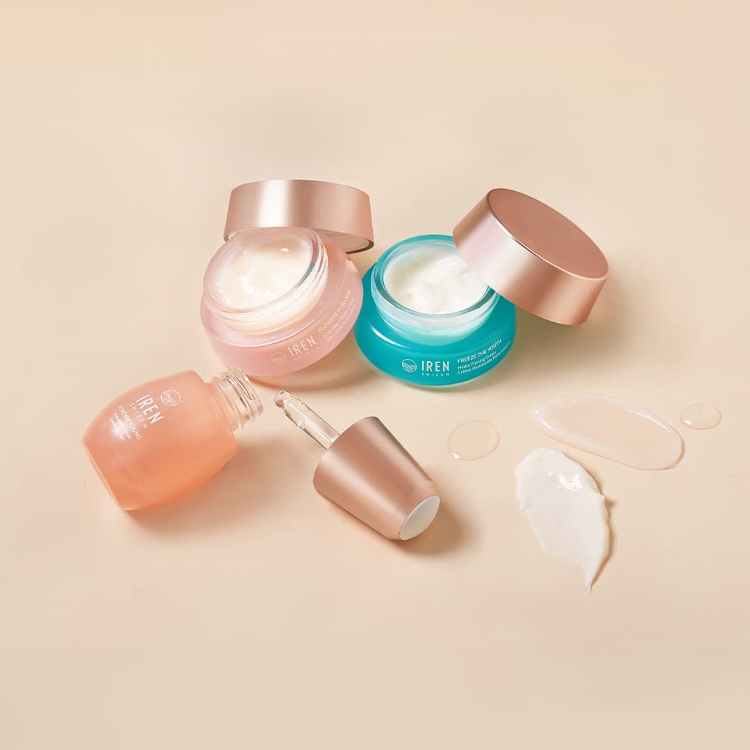 The MOISTURE SANDWICH Skincare Kit by IREN Shizen, featuring pink, blue, and peach containers with visible product smears on a beige surface, showcases hydration and serum absorption. A dropper is placed nearby.